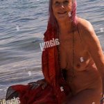 mature nude woman picking up pebbles and shells on the beach Stock Photo